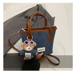 Detail of denim tote bag with brown handles and a cute teddy bear charm pendant
