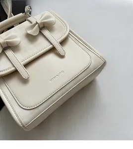 Dettaglio della borsa in ecopelle crema con fiocchi decorativi e logo in argento