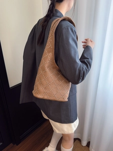 Brown suede shoulder bag with silver studs in a diamond pattern worn by a model