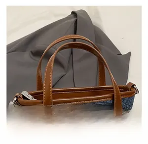 Macro shot of contrast color denim tote with brown leather handles and metal zipper detail