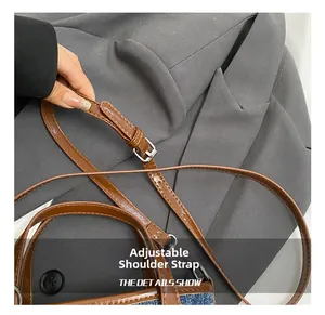 Detail of adjustable brown leather shoulder strap with silver buckle on a denim bucket bag