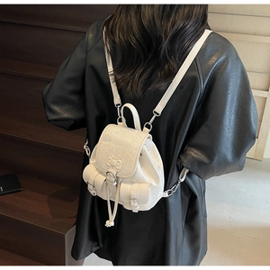 Close-up of white mini backpack with bow detail and side pockets on a leather coat