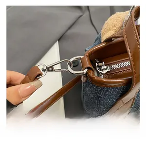 Detail of denim shoulder bag featuring brown leather trim and silver metal hook