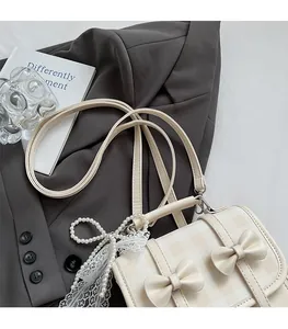 Dettaglio zaino beige con fiocco, patta a quadri e ciondolo elegante in pizzo e perle