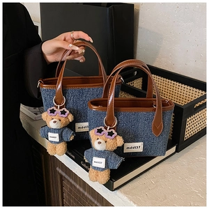 Detail of denim texture tote bag with brown leather handles and teddy bear charm