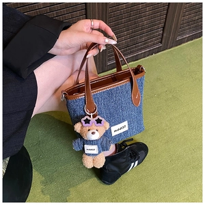 Detail of denim bucket bag with brown leather handles and a cute bear keychain charm