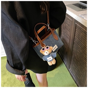 Close-up of blue denim bucket bag with brown leather handles and cute bear charm