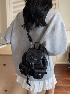 Mini black denim backpack with bow decoration and white dots in a cozy indoor setting