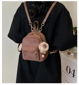 Detail of a brown suede mini backpack with golden zippers and a cute plush animal keychain