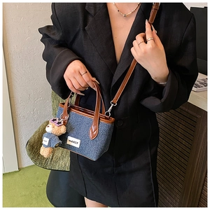 Detail of denim mini tote bag featuring leather handles and cute teddy bear charm accessory