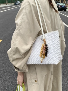 White woven tote bag with wooden bead charm and shoulder strap shown on a model