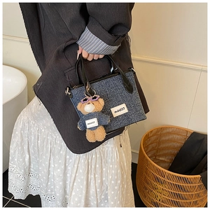 Detail of denim bucket bag with leather handle and teddy bear charm in lifestyle setting