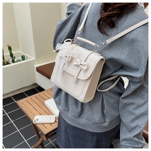 Détail du sac à dos crème avec nœud, texture cuir PU et breloque en dentelle perlée