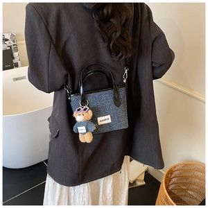 Detail of blue denim bucket bag with designer bear charm and polished black handles