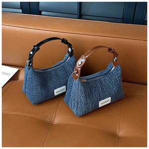 Detail von Denim-Beuteltaschen mit Ledergriffen und Metallbeschlägen auf einem Ledersofa