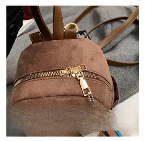 Detail showing golden double zippers and cute plush bear charm on brown suede backpack