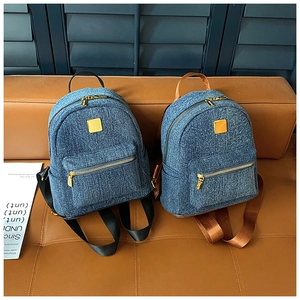Due zaini in denim blu con cerniere dorate su una panca di pelle marrone