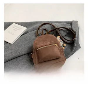 Close-up of brown suede mini backpack with gold zipper and soft decorative fur ball charm