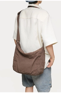 Detailed view of the large capacity brown canvas messenger bag worn by a model