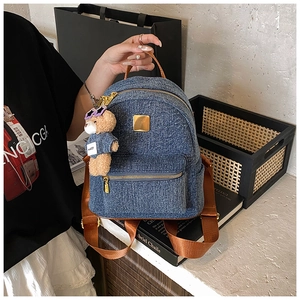 Dettaglio dello zaino in denim blu con manici marroni e ciondolo orsetto viola
