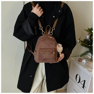 Close-up of brown suede mini backpack with thin straps and plush ball charm on a model