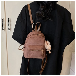 Brown suede mini backpack with plush pompom keychain worn by a model in back view