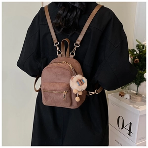 Mini brown faux suede backpack with plush lion charm shown worn by a model in interior
