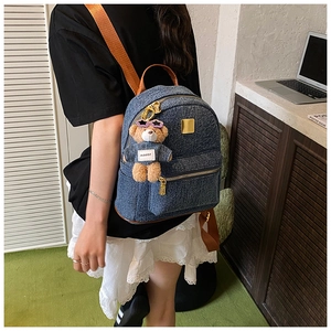 Dettaglio zaino in denim blu con cinturino in pelle marrone e ciondolo a forma di orso