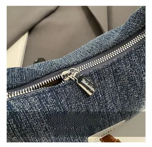 Detailansicht des silbernen Metallreißverschlusses und Markenlogos auf blauer Denimtasche
