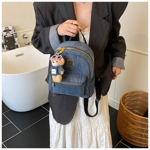 Dettaglio di uno zaino in denim vintage con cerniere dorate e ciondolo a forma di orsetto