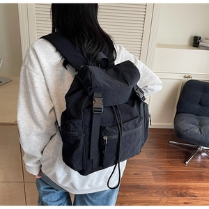 Side view of black canvas backpack with flap buckle closure on male model in modern interior