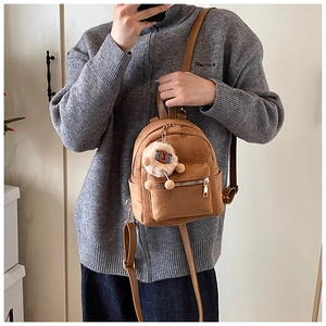 Close-up of a tan suede mini backpack with a plush white lamb charm and gold zippers