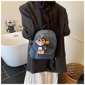 Dettaglio zaino in denim blu scuro con cerniere dorate e ciondolo orsetto di peluche