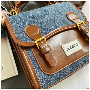 Close-up of blue denim and brown leather patchwork bag with golden buckles and logo tag