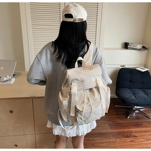 Large cream canvas backpack with flap cover and side pockets on model in a studio