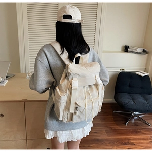 Rear view of a model wearing a large cream canvas backpack in a minimalist study room