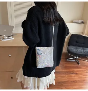 Détail du sac bandoulière gris avec broderies florales et papillons bleus sur tissu texturé