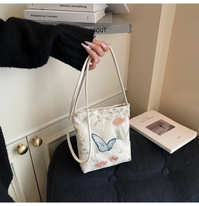 Vue détaillée des broderies papillons bleus et marguerites roses sur sac blanc