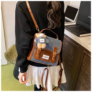 Detailed view of a vintage denim backpack with brown leather straps and plush bear charm