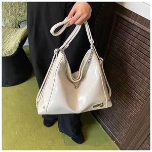 Detail of a creamy white patent leather hobo bag with bold silver chain and adjustable strap