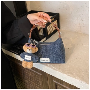 Détail du sac seau en denim avec poignée en cuir et accessoire de charme d'ours
