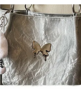 Close-up of silver wrinkled tote bag featuring liquid metal butterfly hardware and fur ball
