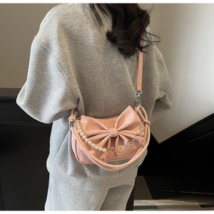Pink bow shoulder bag with pearl chain detail shown on person for size perspective