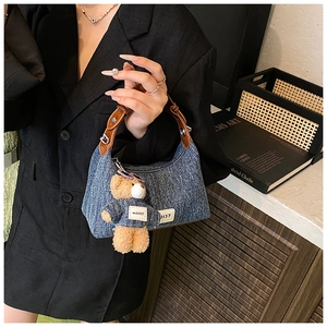 Détail du sac seau en denim bleu avec anse en cuir et un joli porte-clés ourson