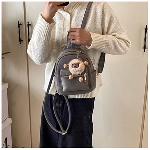 Detail of dark gray mini backpack with matte texture, zippers, and plush sheep charm