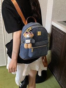 Zaino in denim blu con cinturini in pelle marrone e ciondolo a orsetto sul modello