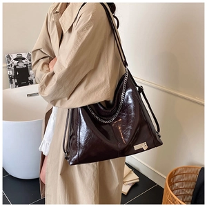 Detailed view of dark brown glossy leather tote featuring silver chain strap and metal logo