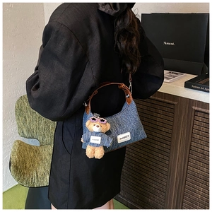 Détail du sac hobo en jean bleu avec poignée en cuir marron et pendentif ours mignon