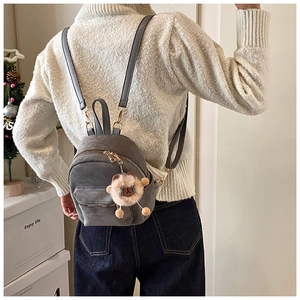 Gray suede mini backpack with plush alpaca charm shown on model in cozy home setting