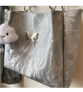 Close-up of silver tote bag with metallic butterfly charm and white cloud pendant